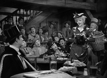 Movie still from “The Picture of Dorian Gray” (1945), directed by Albert Lewin – A group of people sitting in a room with a woman in a hat; Wide shot, Over the shoulder angle