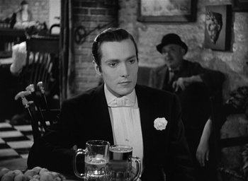 Movie still from “The Picture of Dorian Gray” (1945), directed by Albert Lewin – A black and white photo of a man sitting at a table with two beers; Medium shot, Over the shoulder angle