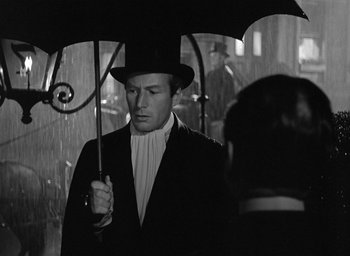 Movie still from “The Picture of Dorian Gray” (1945), directed by Albert Lewin – A man holding an umbrella while standing in the rain; Medium shot, Over the shoulder angle