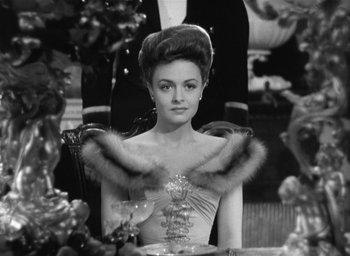 Movie still from “The Picture of Dorian Gray” (1945), directed by Albert Lewin – A woman sitting at a dinner table wearing a dress; Medium shot, Over the shoulder angle