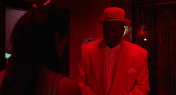 Movie still from “The Players Club” (1998), directed by Ice Cube – A man wearing a red suit and a hat; Medium shot, Over the shoulder angle