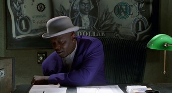 Movie still from “The Players Club” (1998), directed by Ice Cube – A man sitting at a table in front of a dollar bill; Medium shot, Low angle