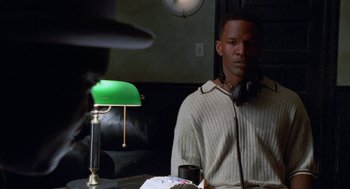Movie still from “The Players Club” (1998), directed by Ice Cube – A man sitting in front of a green lamp in a room; Medium shot, Over the shoulder angle