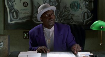 Movie still from “The Players Club” (1998), directed by Ice Cube – A man sitting at a table in front of money; Medium shot, Low angle
