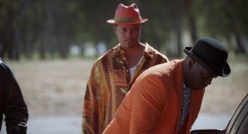 Movie still from “The Players Club” (1998), directed by Ice Cube – A man in an orange hat is standing next to another man in an orange jacket; Medium shot, Over the shoulder angle