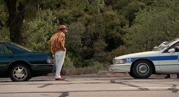 Movie still from “The Players Club” (1998), directed by Ice Cube – A man standing in the middle of the road next to a cop car; Wide shot, Low angle