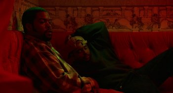 Movie still from “The Players Club” (1998), directed by Ice Cube – A couple of men sitting on top of a red couch; Medium shot, High angle