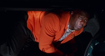 Movie still from “The Players Club” (1998), directed by Ice Cube – A man in an orange jacket looking down at the ground; Medium shot, Low angle