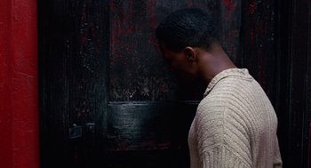Movie still from “The Players Club” (1998), directed by Ice Cube – A man in a white sweater standing in front of a door; Close Up shot, High angle