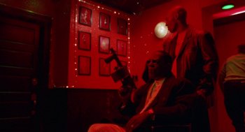 Movie still from “The Players Club” (1998), directed by Ice Cube – A man sitting in a chair in a red room; Medium shot, Low angle