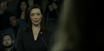 Movie still from “House of Cards” (2013), created by Beau Willimon – A woman in a black jacket is standing in front of a microphone; Close Up shot, Over the shoulder angle
