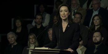 Movie still from “House of Cards” (2013), created by Beau Willimon – A woman standing at a podium speaking to a crowd of onlookers; Medium shot, Over the shoulder angle
