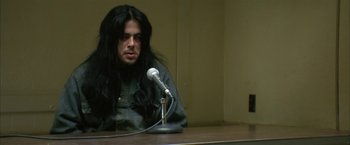 Movie still from “The Pledge” (2001), directed by Sean Penn – A man sitting at a table in front of a microphone; Close Up shot, Low angle