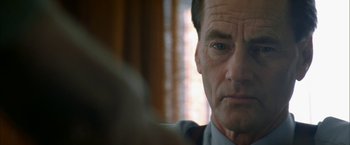 Movie still from “The Pledge” (2001), directed by Sean Penn – An older man looking at the camera in a room; Close Up shot, Over the shoulder angle