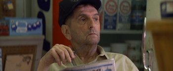 Movie still from “The Pledge” (2001), directed by Sean Penn – An older man holding a newspaper while wearing a hat; Close Up shot, Low angle