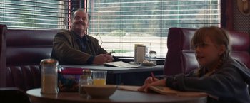 Movie still from “The Pledge” (2001), directed by Sean Penn – A man sitting at a table in front of a woman; Medium shot, Over the shoulder angle