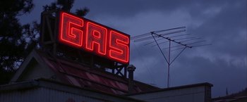 Movie still from “The Pledge” (2001), directed by Sean Penn – A gas sign on the side of a building lit up at night; Extreme Wide shot, Low angle