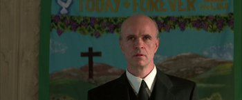 Movie still from “The Pledge” (2001), directed by Sean Penn – A man in a suit and tie in front of a cross; Close Up shot, Low angle