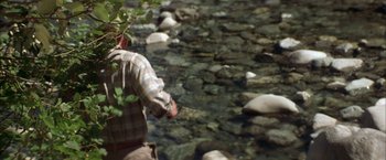 Movie still from “The Pledge” (2001), directed by Sean Penn – A man holding a plant next to a body of water; Medium shot, High angle