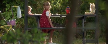 Movie still from “The Pledge” (2001), directed by Sean Penn – A little girl in a red dress sitting on a park bench; Medium shot, Low angle