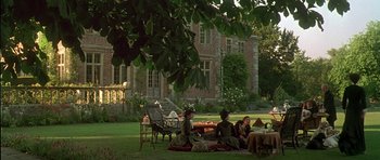 Movie still from “The Portrait of a Lady” (1996), directed by Jane Campion – A group of people sitting in the grass near a building; Extreme Wide shot, High angle