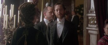 Movie still from “The Portrait of a Lady” (1996), directed by Jane Campion – A man in a tuxedo standing next to another man in a suit; Medium shot, Over the shoulder angle