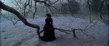Movie still from “The Portrait of a Lady” (1996), directed by Jane Campion – A woman in a black dress standing next to a tree in the snow; Wide shot, High angle