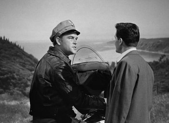 Movie still from “The Postman Always Rings Twice” (1946), directed by Tay Garnett – A man wearing a leather jacket and a hat is talking to another man; Medium shot, Over the shoulder angle