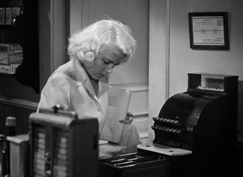 Movie still from “The Postman Always Rings Twice” (1946), directed by Tay Garnett – An old black and white photo of a woman at a cash register; Medium shot, Low angle
