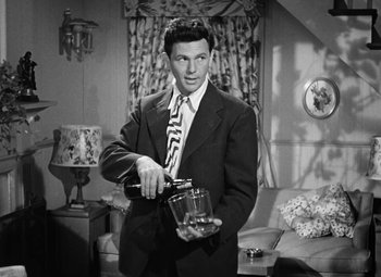 Movie still from “The Postman Always Rings Twice” (1946), directed by Tay Garnett – A black and white photo of a man in a suit and tie holding a glass; Medium shot, Low angle