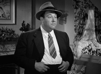 Movie still from “The Postman Always Rings Twice” (1946), directed by Tay Garnett – A black and white photo of a man in a suit and hat; Medium shot, Low angle