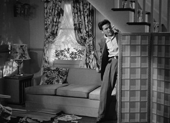 Movie still from “The Postman Always Rings Twice” (1946), directed by Tay Garnett – A black and white photo of a man leaning on a couch; Wide shot, High angle