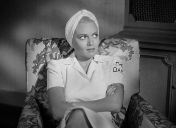 Movie still from “The Postman Always Rings Twice” (1946), directed by Tay Garnett – A black and white photo of a woman sitting in a chair with her arms crossed; Close Up shot, High angle