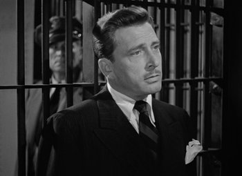 Movie still from “The Postman Always Rings Twice” (1946), directed by Tay Garnett – A black and white photo of a man in a suit and tie in front of a jail cell; Close Up shot, Low angle