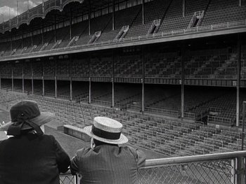 Movie still from “The Pride of the Yankees” (1942), directed by Sam Wood – Two men in hats are sitting in a stadium; Extreme Wide shot, High angle