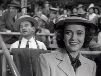 Movie still from “The Pride of the Yankees” (1942), directed by Sam Wood – A woman wearing a suit and a hat in front of an audience; Medium shot, Low angle