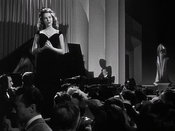 Movie still from “The Pride of the Yankees” (1942), directed by Sam Wood – A woman standing in front of an audience in front of a piano; Medium shot, Low angle