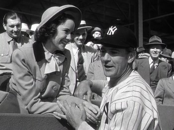 Movie still from “The Pride of the Yankees” (1942), directed by Sam Wood – A man and a woman sitting next to each other at a baseball game; Medium shot, Low angle