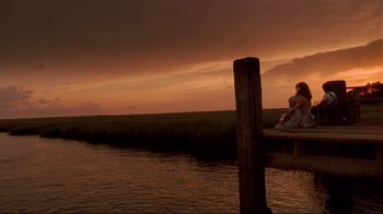 Movie still from “The Prince of Tides” (1991), directed by Barbra Streisand – Two people sitting on a dock watching the sunset; Extreme Wide shot, Low angle