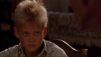 Movie still from “The Prince of Tides” (1991), directed by Barbra Streisand – A young boy sitting in front of a wooden chair; Close Up shot, Over the shoulder angle