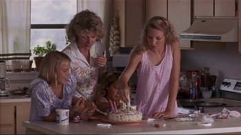 Movie still from “The Prince of Tides” (1991), directed by Barbra Streisand – A group of people standing around a table with a cake; Medium shot, High angle