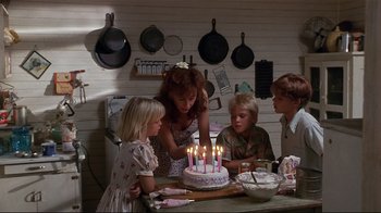 Movie still from “The Prince of Tides” (1991), directed by Barbra Streisand – A group of people standing around a cake with lit candles; Medium shot, High angle