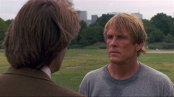 Movie still from “The Prince of Tides” (1991), directed by Barbra Streisand – A man with blonde hair and a gray t - shirt talking to another man in a field; Close Up shot, Over the shoulder angle