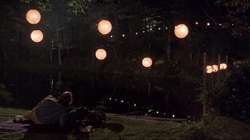 Movie still from “The Prince of Tides” (1991), directed by Barbra Streisand – A person sitting on the ground near a body of water; Wide shot, High angle