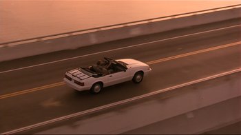 Movie still from “The Prince of Tides” (1991), directed by Barbra Streisand – A white car driving down a street next to a bridge; Wide shot, High angle
