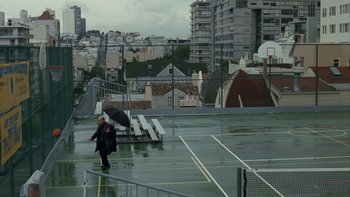 Movie still from “The Princess Diaries” (2001), directed by Garry Marshall – A person holding an umbrella while standing on a tennis court; Extreme Wide shot, High angle