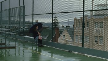 Movie still from “The Princess Diaries” (2001), directed by Garry Marshall – A woman holding an umbrella while sitting on a ledge; Wide shot, High angle