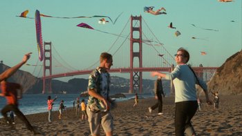 Movie still from “The Princess Diaries” (2001), directed by Garry Marshall – A group of people on a beach flying kites; Extreme Wide shot, Over the shoulder angle