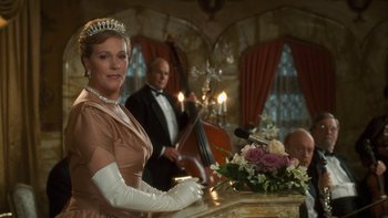 A woman wearing a tiara stands in front of a table with flowers