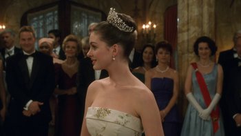Movie still from “The Princess Diaries” (2001), directed by Garry Marshall – A woman wearing a tiara in front of a group of people; Close Up shot, Over the shoulder angle